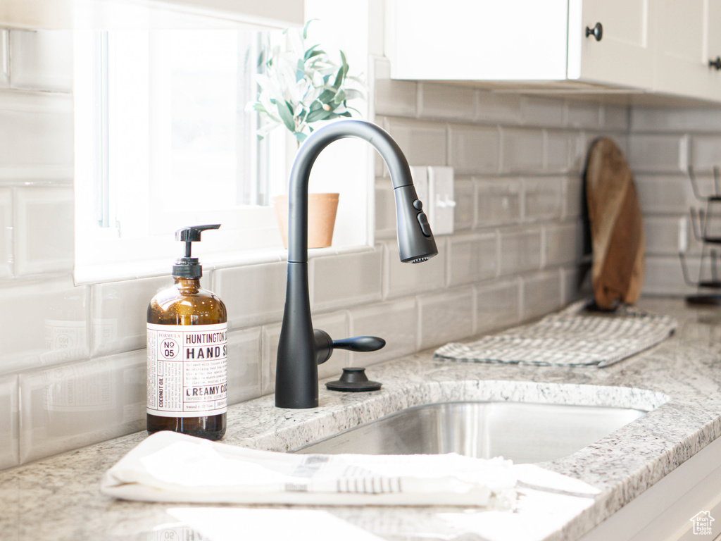 Interior details with white cabinetry, a sink, light stone countertops, and decorative backsplash