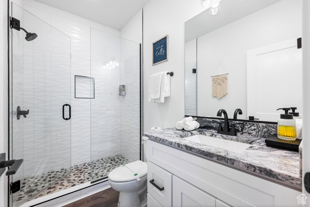 Bathroom with hardwood / wood-style floors, vanity, toilet, and a shower with door