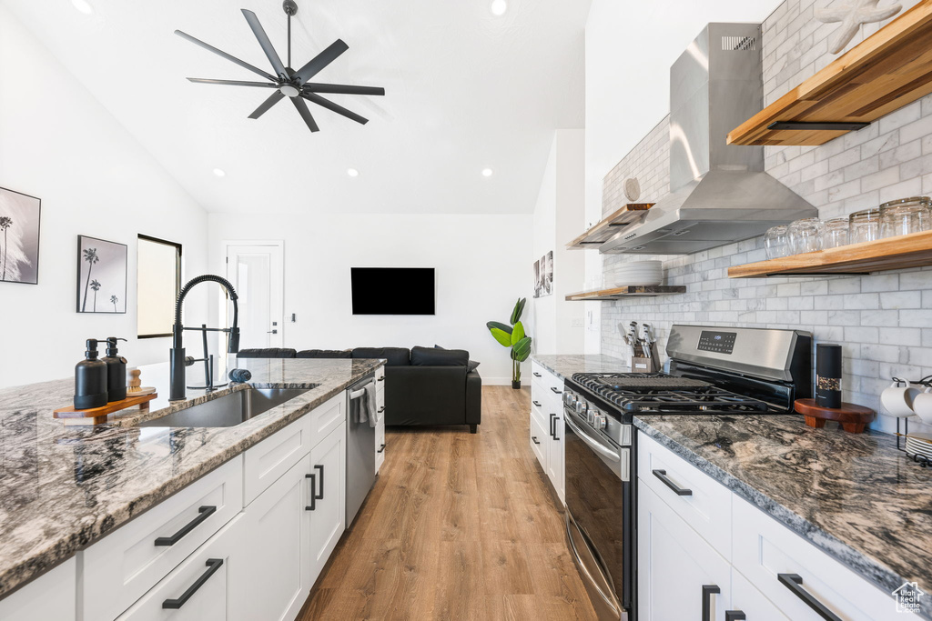 Kitchen with white cabinetry, sink, wall chimney range hood, light hardwood / wood-style flooring, and appliances with stainless steel finishes