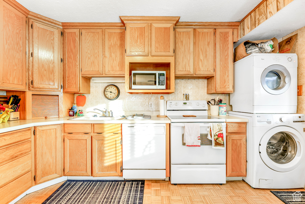 Kitchen featuring white appliances, light parquet floors, stacked washer / dryer, and sink
