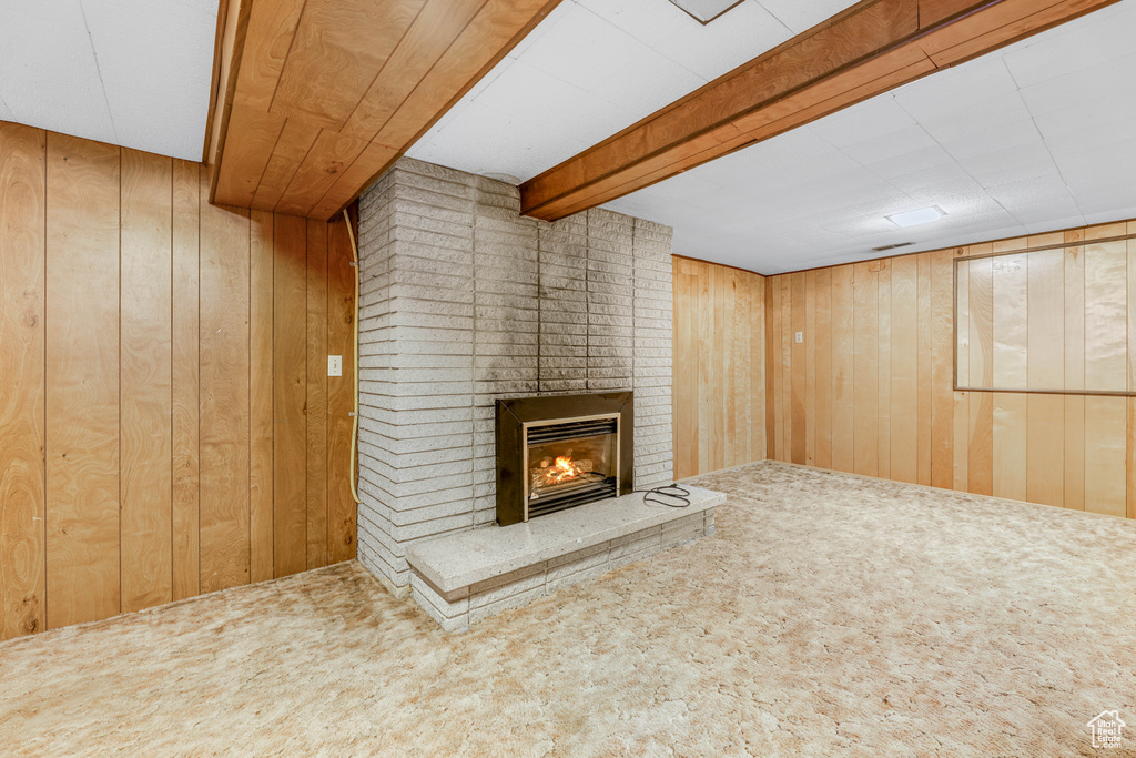 Unfurnished living room featuring carpet, a fireplace, wooden walls, and beamed ceiling