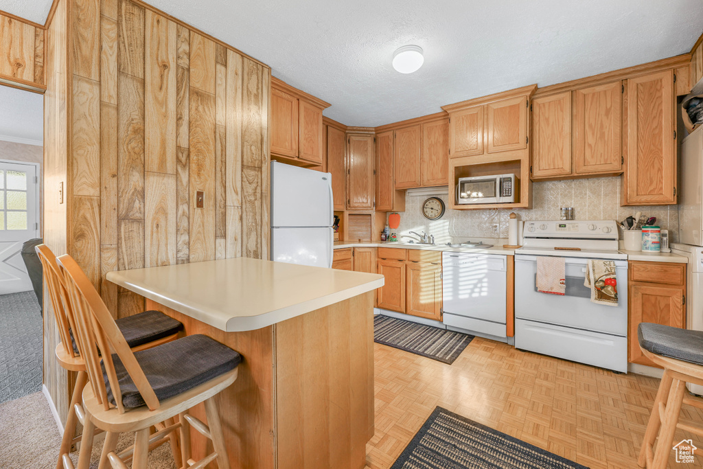 Kitchen featuring light parquet floors, a textured ceiling, white appliances, decorative backsplash, and a breakfast bar