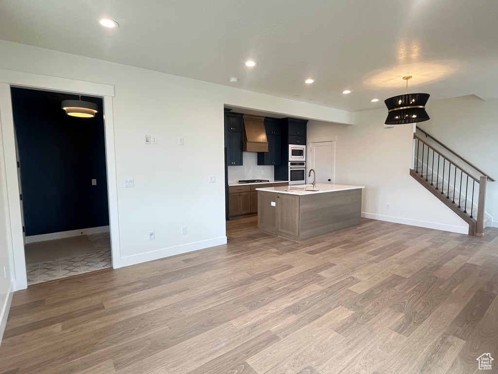 Kitchen featuring custom exhaust hood, light countertops, light wood finished floors, and stainless steel appliances