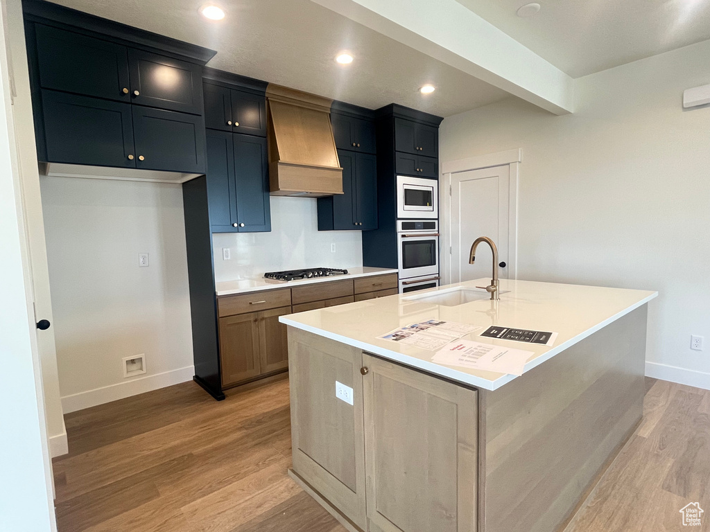 Kitchen featuring custom range hood, light wood-style floors, gas stovetop, white oven, and a sink