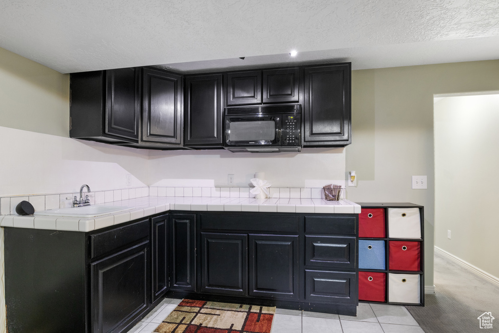 Kitchen featuring tile countertops, sink, light tile patterned floors, and a textured ceiling
