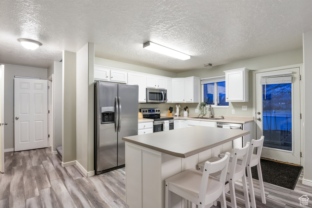 Kitchen with white cabinets, sink, a textured ceiling, appliances with stainless steel finishes, and light hardwood / wood-style floors
