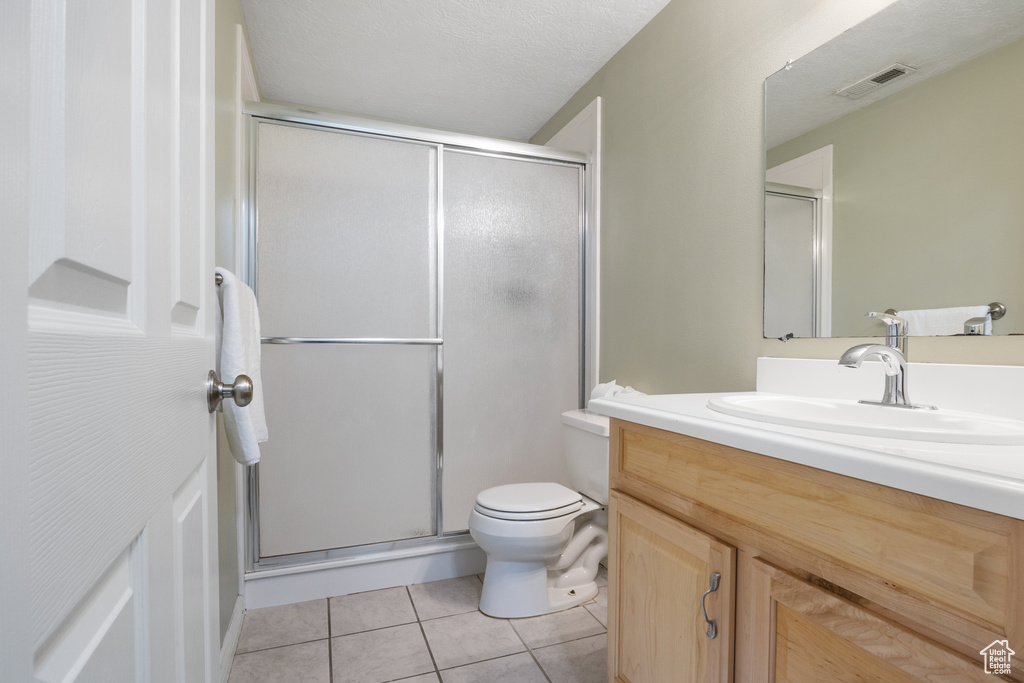 Bathroom featuring tile patterned floors, a textured ceiling, toilet, vanity, and a shower with shower door