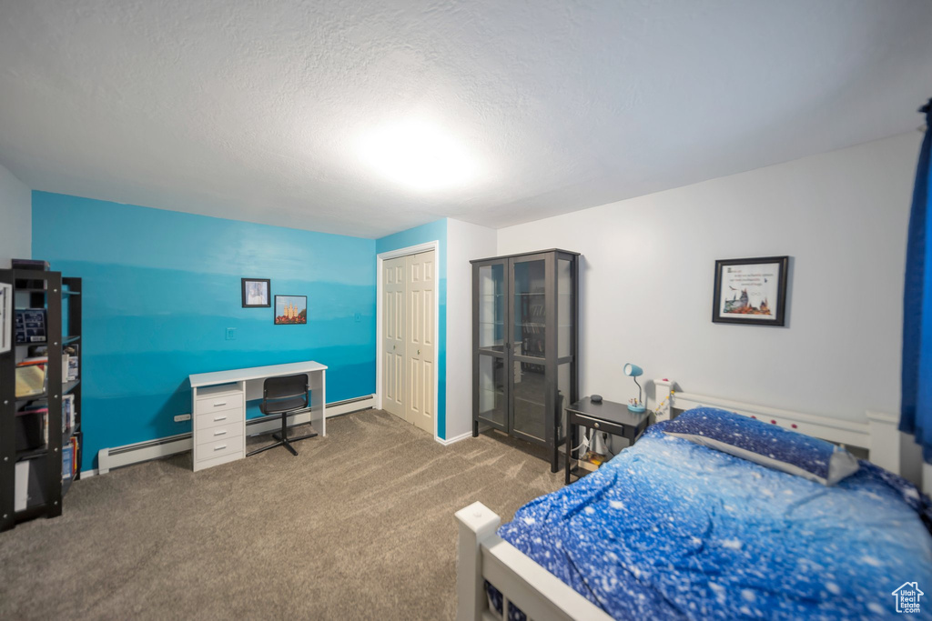 Bedroom with carpet flooring, a baseboard heating unit, a textured ceiling, and a closet