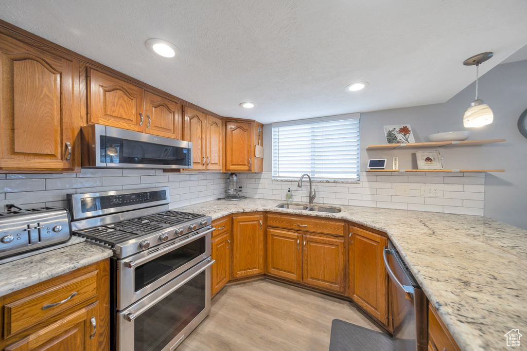 Kitchen featuring light hardwood / wood-style floors, light stone countertops, sink, and appliances with stainless steel finishes