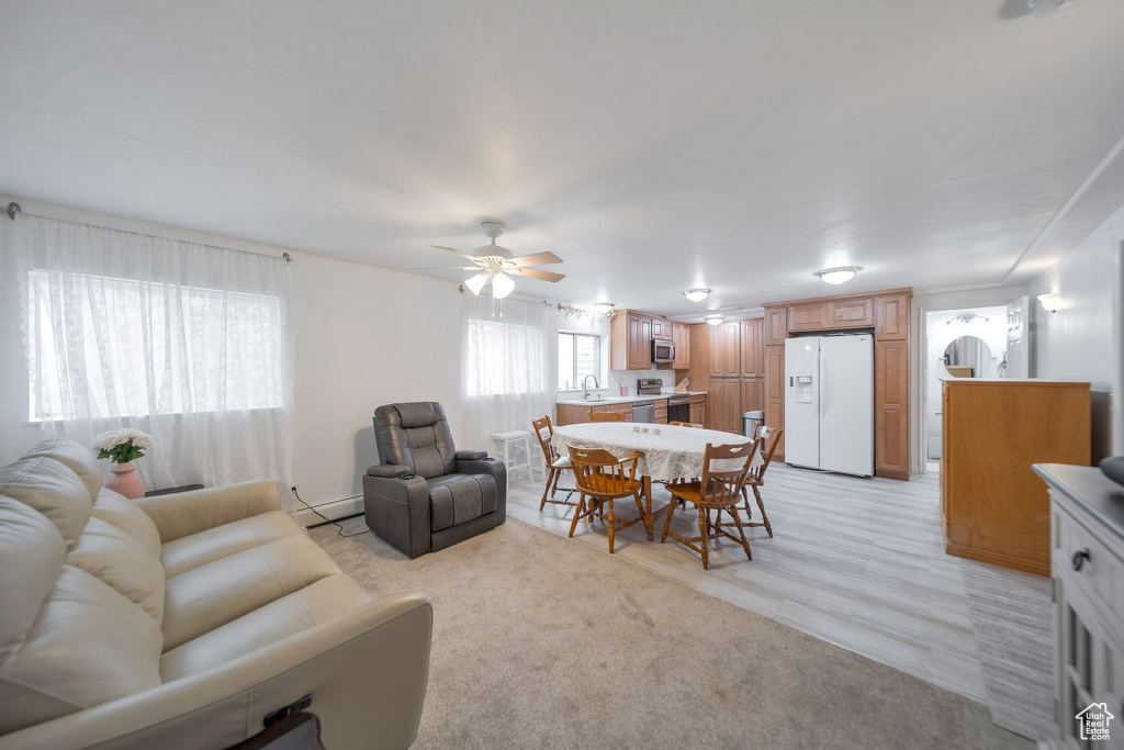 Living room featuring light carpet, baseboard heating, ceiling fan, and sink