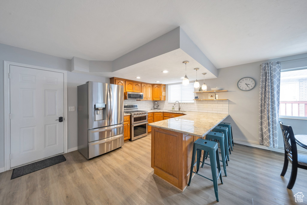 Kitchen featuring sink, kitchen peninsula, a breakfast bar area, appliances with stainless steel finishes, and light wood-type flooring