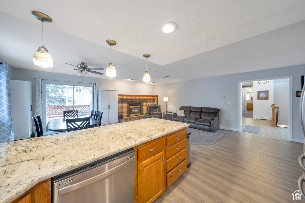 Kitchen featuring light stone countertops, a fireplace, ceiling fan, dishwasher, and light hardwood / wood-style floors