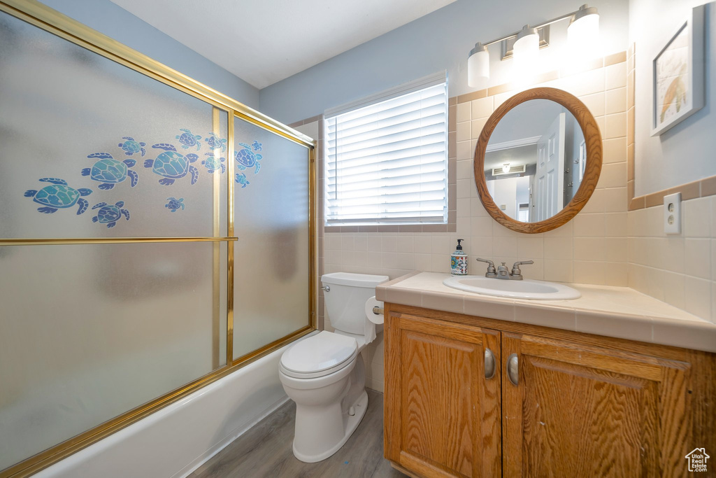Full bathroom with vanity, combined bath / shower with glass door, toilet, tile walls, and wood-type flooring