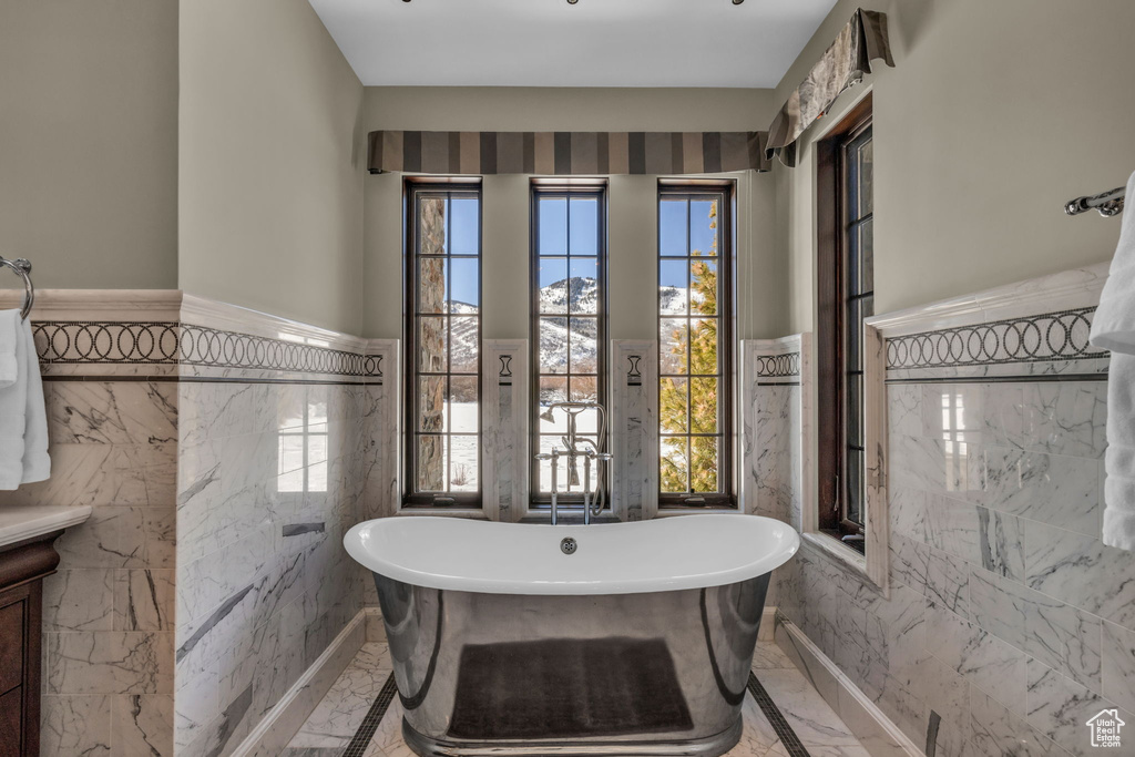 Bathroom with a washtub, a healthy amount of sunlight, and tile walls