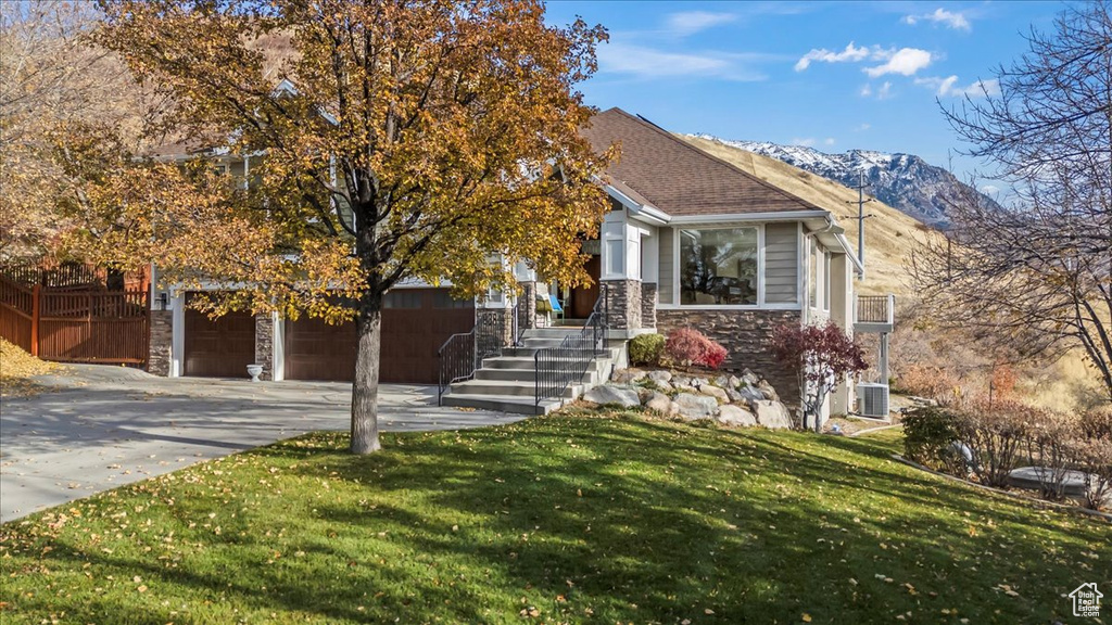 View of front of home with a mountain view, a garage, central AC unit, and a front yard