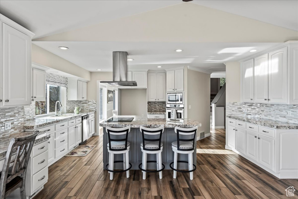 Kitchen featuring decorative backsplash, appliances with stainless steel finishes, island range hood, white cabinets, and lofted ceiling