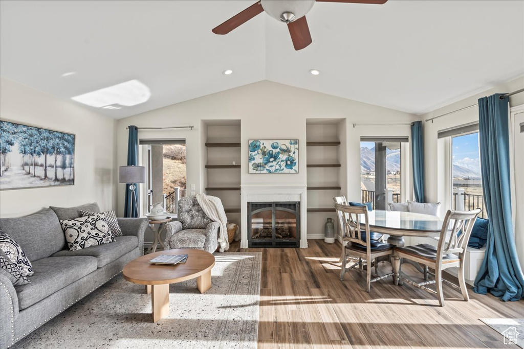 Living room featuring ceiling fan, built in features, wood-type flooring, and vaulted ceiling