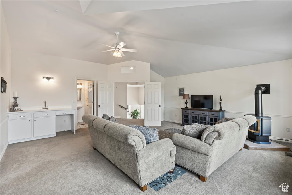 Carpeted living room featuring vaulted ceiling, a wood stove, and ceiling fan