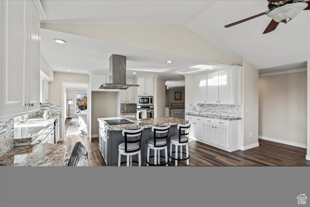 Kitchen with island exhaust hood, light stone counters, a center island, and white cabinets