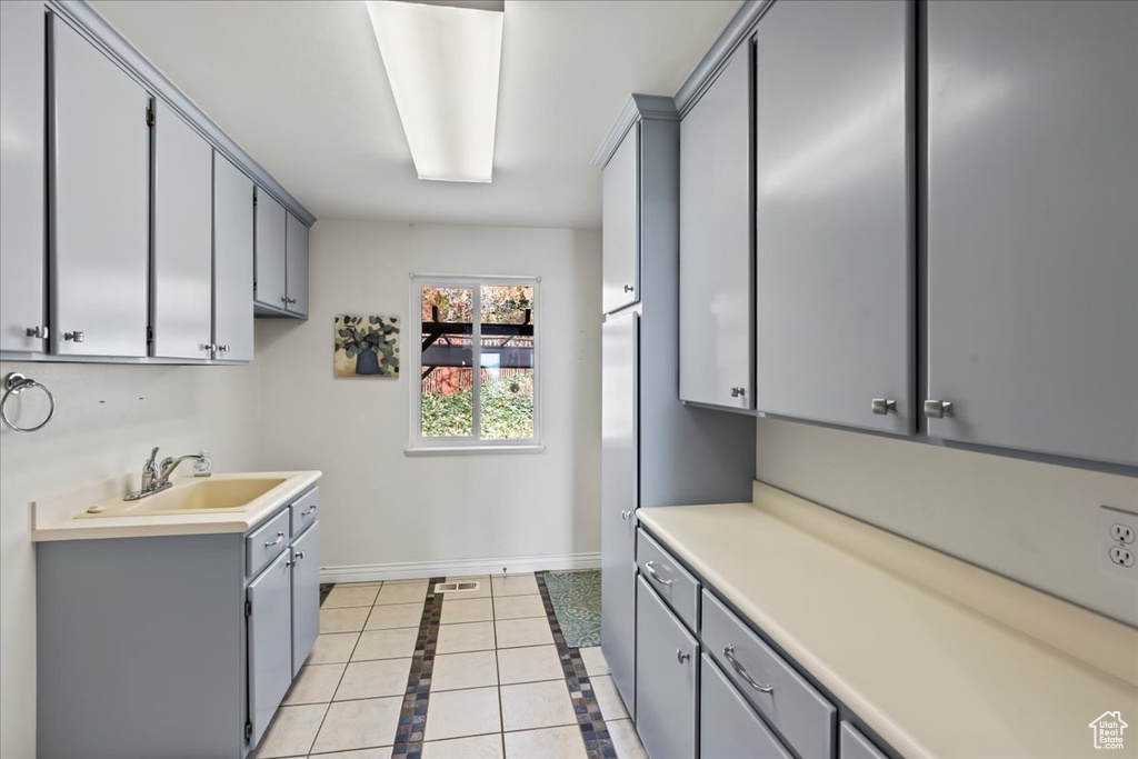 Kitchen with gray cabinetry, light tile patterned floors, and sink