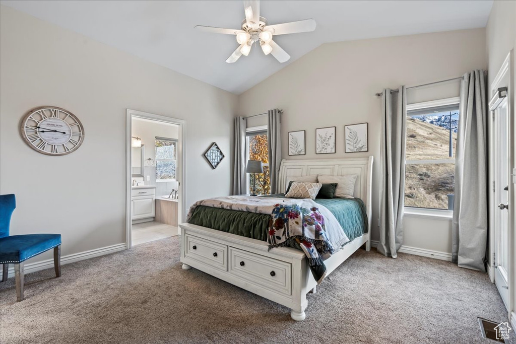 Carpeted bedroom with multiple windows, ceiling fan, ensuite bath, and vaulted ceiling