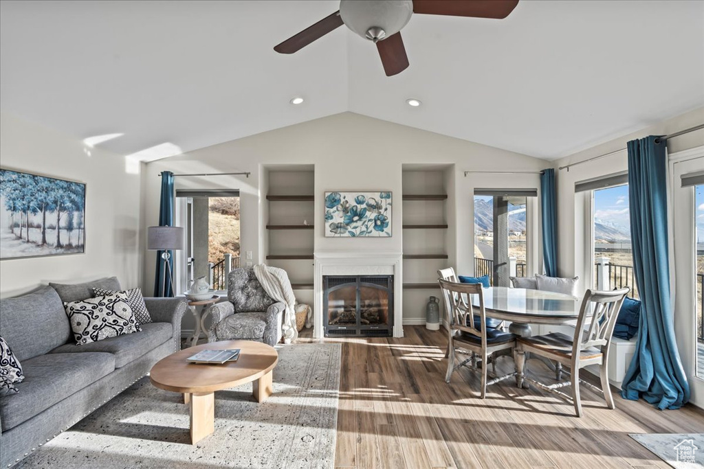 Living room with hardwood / wood-style flooring, ceiling fan, built in features, and lofted ceiling