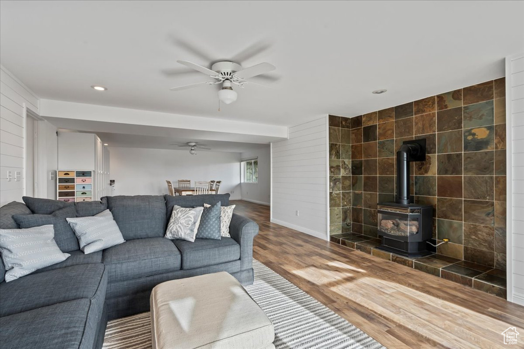 Living room featuring hardwood / wood-style floors, a wood stove, tile walls, and ceiling fan