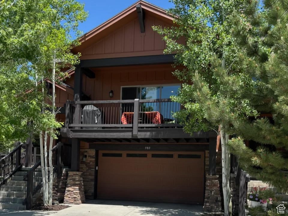 View of front of home featuring an attached garage, concrete driveway, board and batten siding, and a balcony