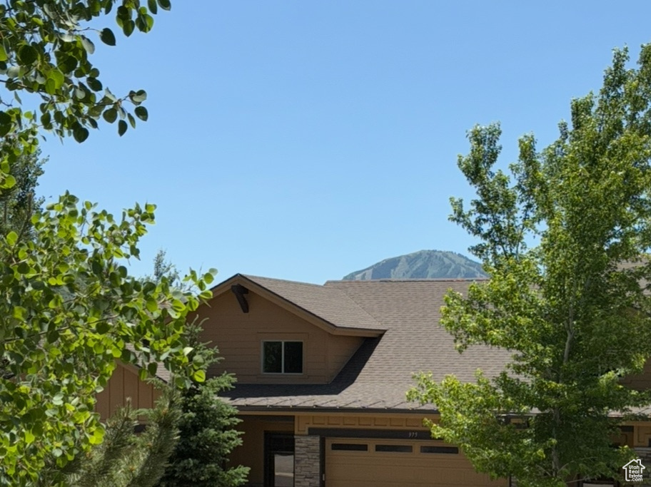 View of front of home with stone siding, concrete driveway, an attached garage, and roof with shingles