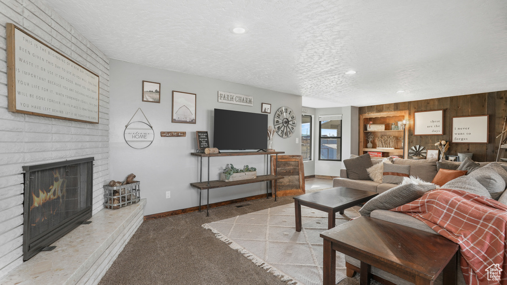 Living room featuring wooden walls, light colored carpet, a textured ceiling, and a brick fireplace