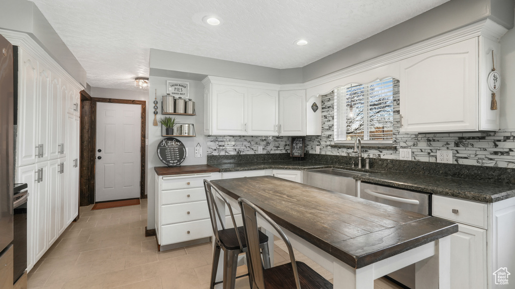 Kitchen featuring white cabinets, decorative backsplash, light tile patterned flooring, and sink