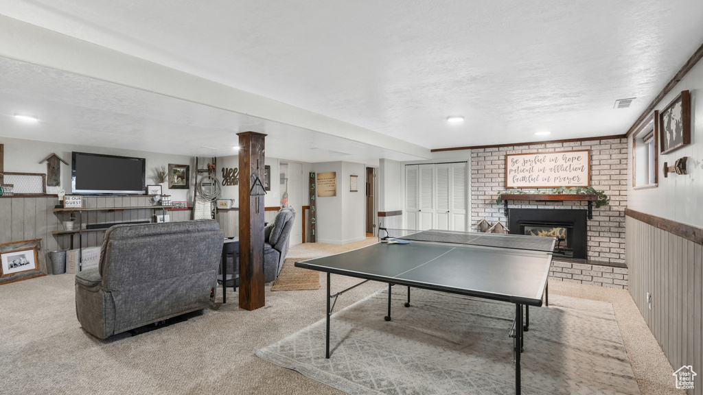 Playroom with wooden walls, light colored carpet, a textured ceiling, and a brick fireplace