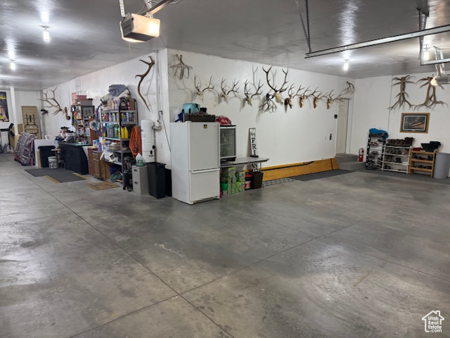 Garage with white refrigerator, a garage door opener, and a workshop area