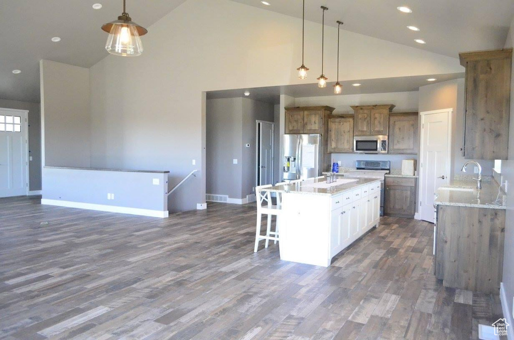 Kitchen featuring high vaulted ceiling, stainless steel appliances, a center island with sink, and light stone countertops