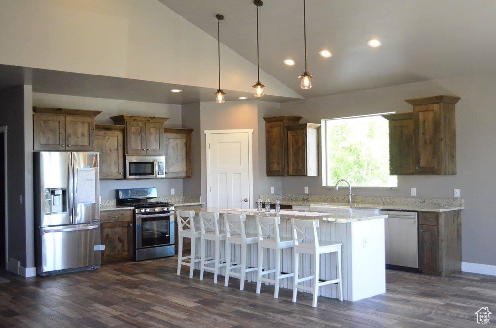 Kitchen featuring a center island with sink, light stone counters, appliances with stainless steel finishes, and dark wood-type flooring