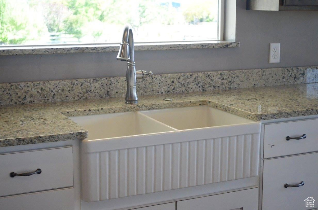 Interior details with sink, white cabinets, and light stone countertops