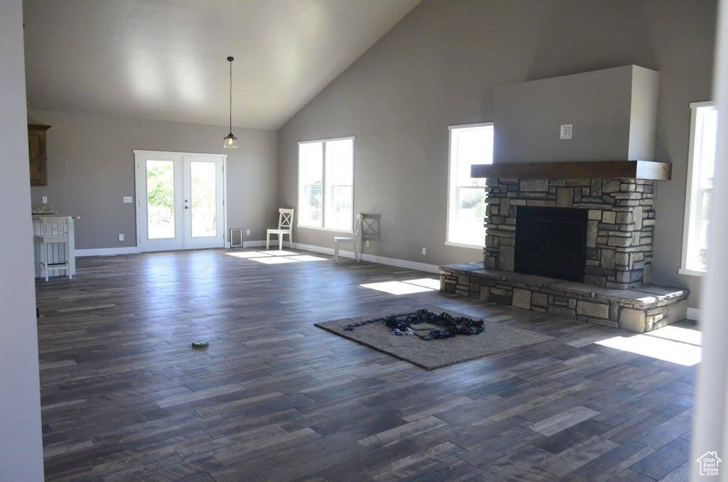 Unfurnished living room featuring high vaulted ceiling, a stone fireplace, french doors, and dark hardwood / wood-style flooring