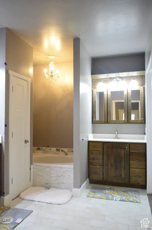 Bathroom with tiled bath, tile patterned floors, vanity, and an inviting chandelier