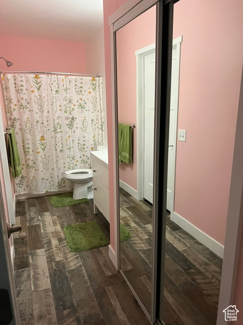 Bathroom with hardwood / wood-style floors, a shower with curtain, toilet, and vanity