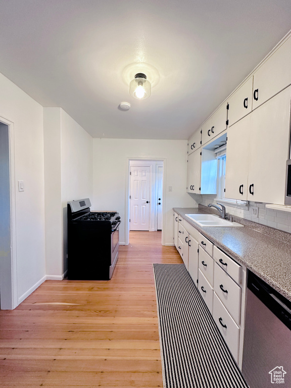 Kitchen with sink, black gas range oven, light hardwood / wood-style flooring, stainless steel dishwasher, and white cabinets