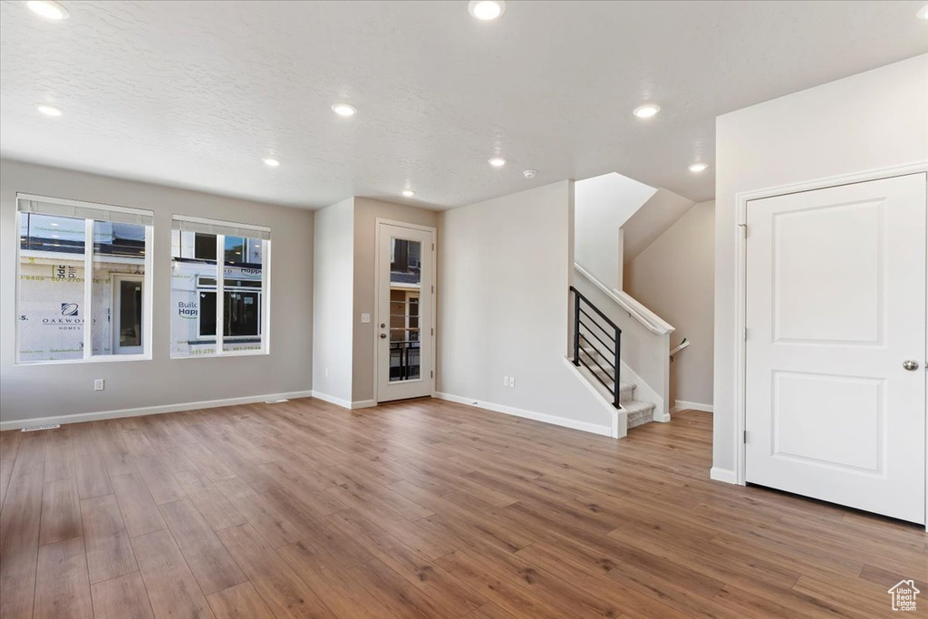Unfurnished living room with a textured ceiling, baseboards, wood finished floors, recessed lighting, and stairway