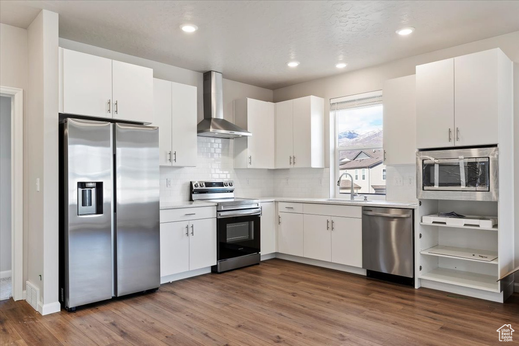Kitchen featuring a sink, wall chimney range hood, stainless steel appliances, and dark wood finished floors