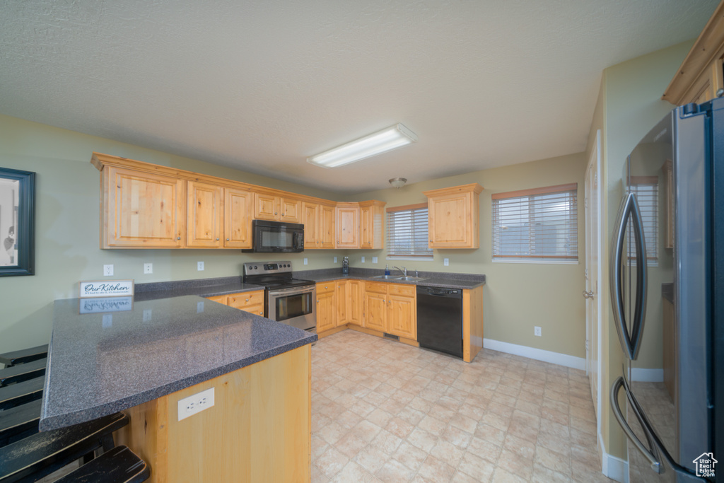 Kitchen with black appliances, light brown cabinets, kitchen peninsula, and sink