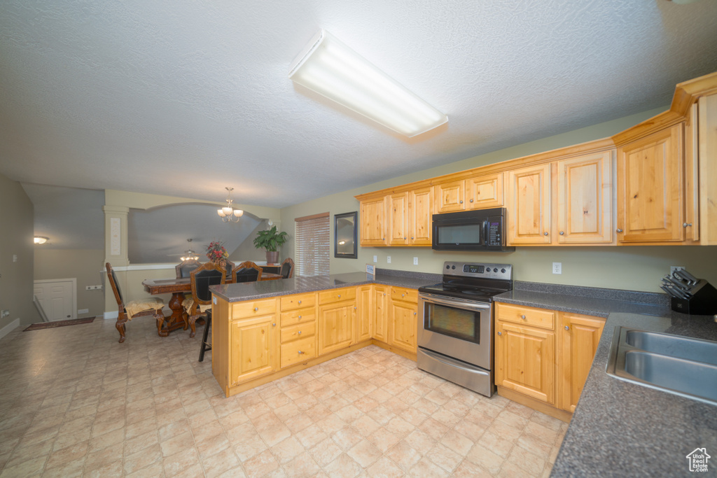 Kitchen with kitchen peninsula, decorative columns, sink, electric stove, and a notable chandelier