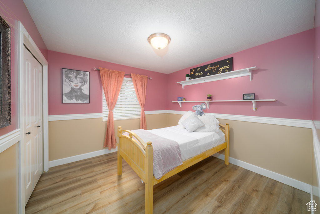 Bedroom with hardwood / wood-style floors, a textured ceiling, and a closet