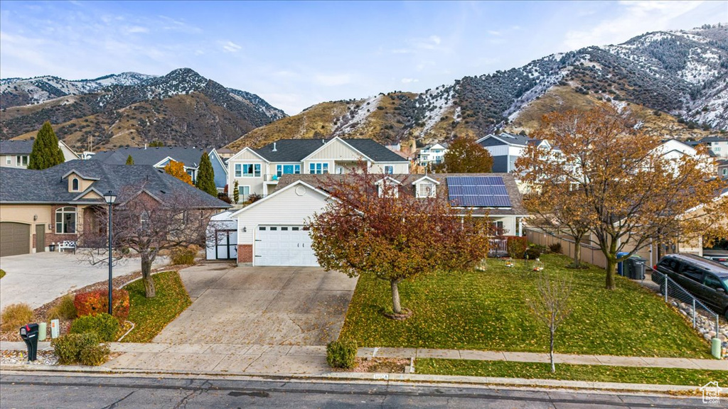 View of property featuring a mountain view, a front lawn, a garage, and solar panels