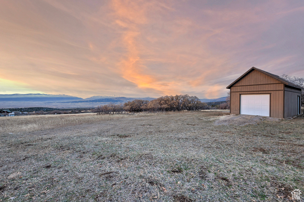 Yard at dusk with a mountain view, a garage, and an outdoor structure