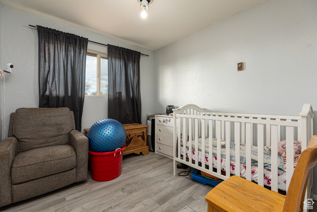 Bedroom with a crib, light hardwood / wood-style flooring, and vaulted ceiling