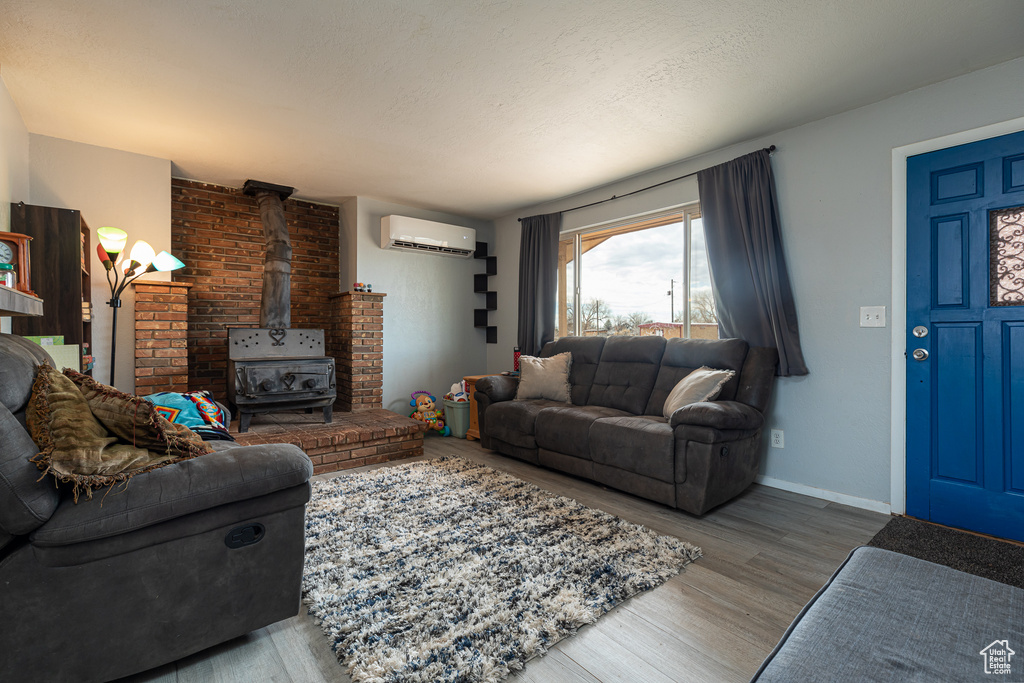 Living room featuring a wall mounted air conditioner, a textured ceiling, hardwood / wood-style flooring, and a wood stove