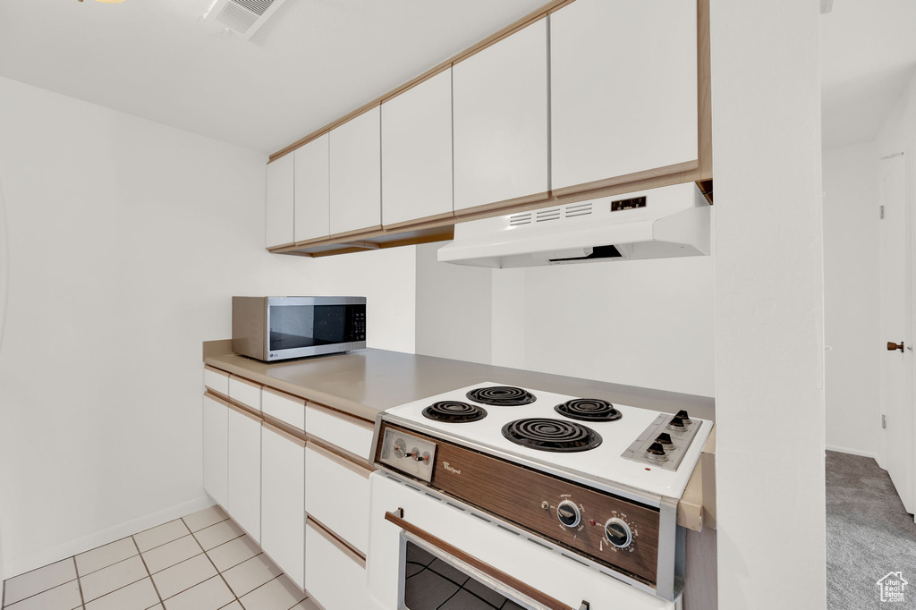 Kitchen featuring light tile patterned floors, white cabinetry, and white stovetop